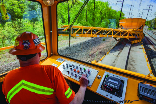 Crews are upgrading track between Washington Union and Baltimore Penn stations. The casting equipment car operator is supervising work of the spoil casting.