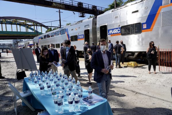 Attendees are offered water and fact sheets as they exit the shuttle train to the event site.