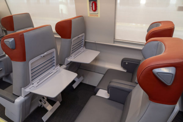 The color ‘red’ distinguishes First Class from Business Class - as evident in the headrests here, and also on the door to the trainset. These First Class seats provide more space, leg room and personal tray tables, that can remain open or closed independent from one’s neighbor.