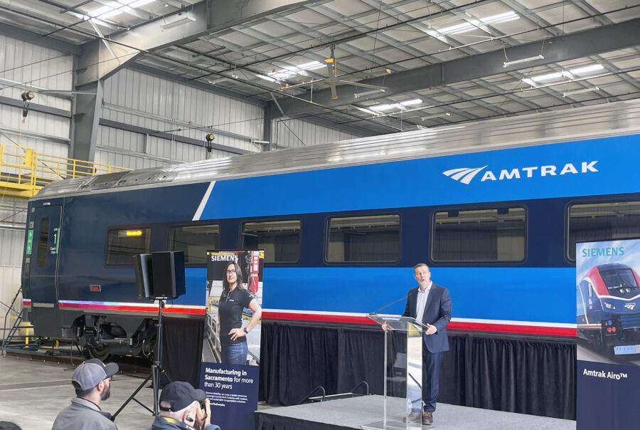 Amtrak President Roger Harris speaks at a podium in front of a new Amtrak Airo train