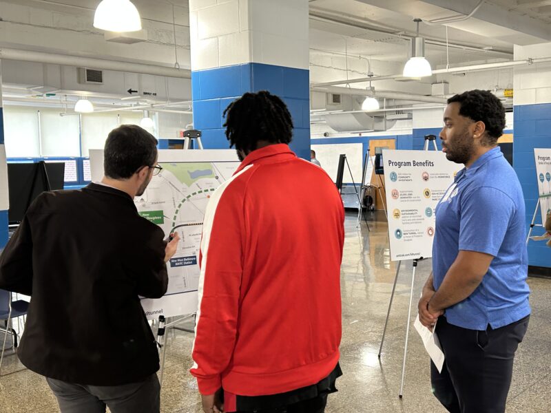 Community members speak with members of the Frederick Douglass Tunnel Program next to a map of the project