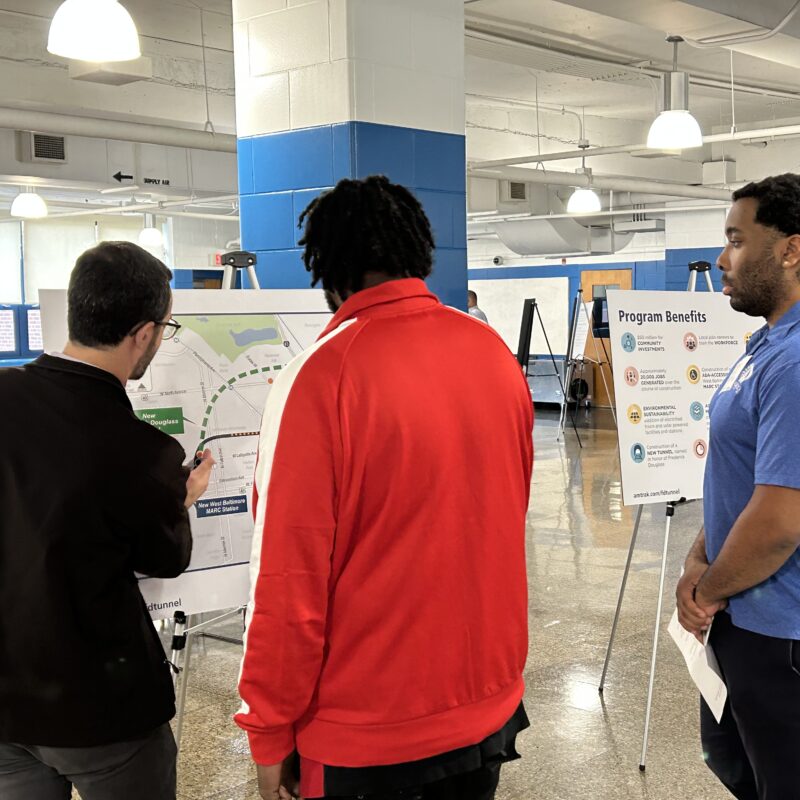 Community members speak with members of the Frederick Douglass Tunnel Program next to a map of the project