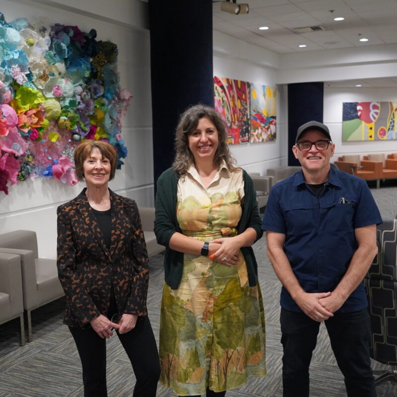 Three people standing in a room. Artwork on the wall.