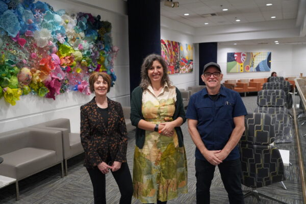 Three people standing in a room. Artwork on the wall.