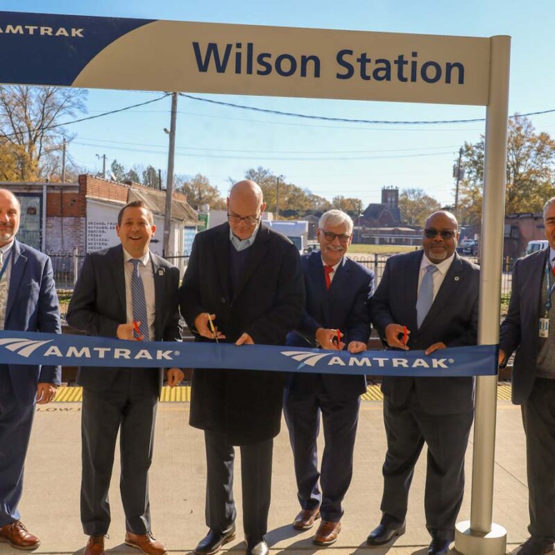 Group of people standing near ribbon and sign.