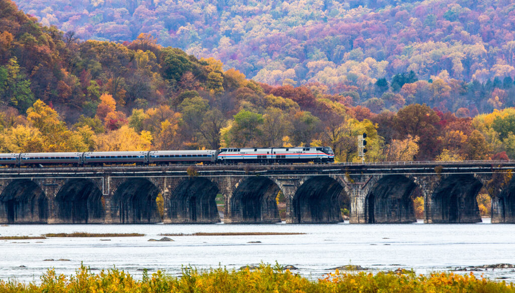 Amtrak train on bridge with fall colors in the background.