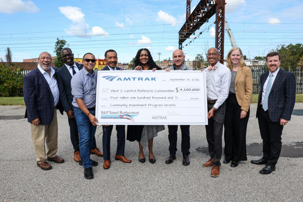 Multiple VIPs representing Amtrak, Congress, and state and local elected officials holding a large check committing 4.1 million dollars to the West and Central Baltimore communities
